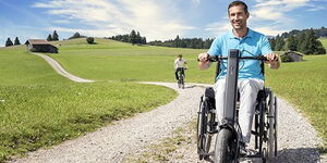 Manueller Rollstuhl mit einem Zuggerät auf einem Schotterweg in der Natur